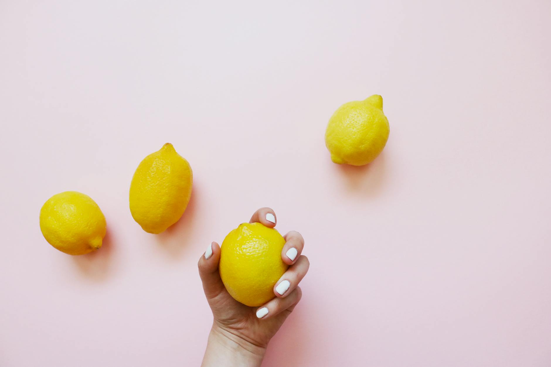 A hand holding a lemon on a soft pink background, symbolizing gentle touch and renewed sensation