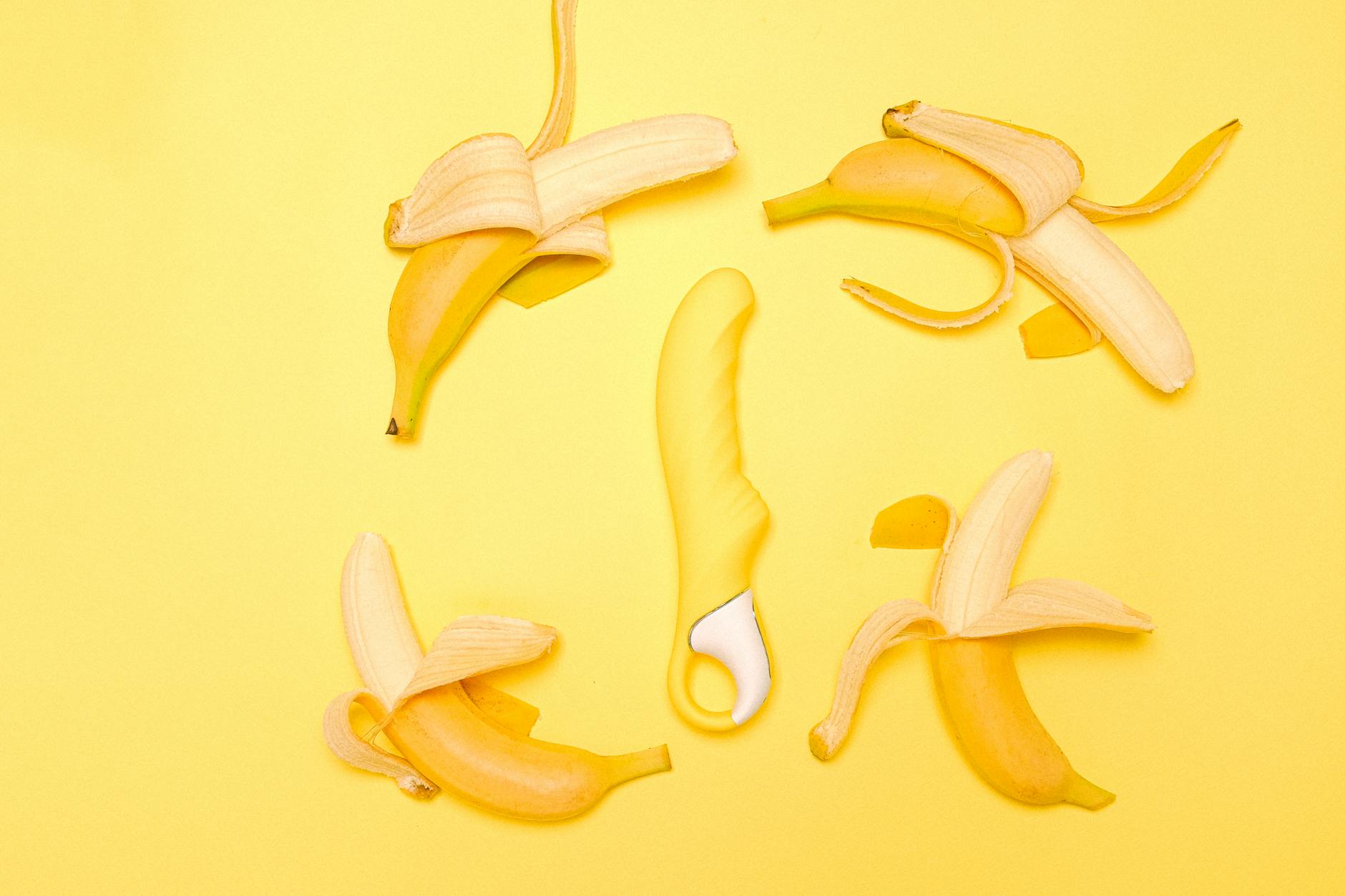 A yellow silicone clitoral vibrator on a yellow background surrounded by fresh fruit