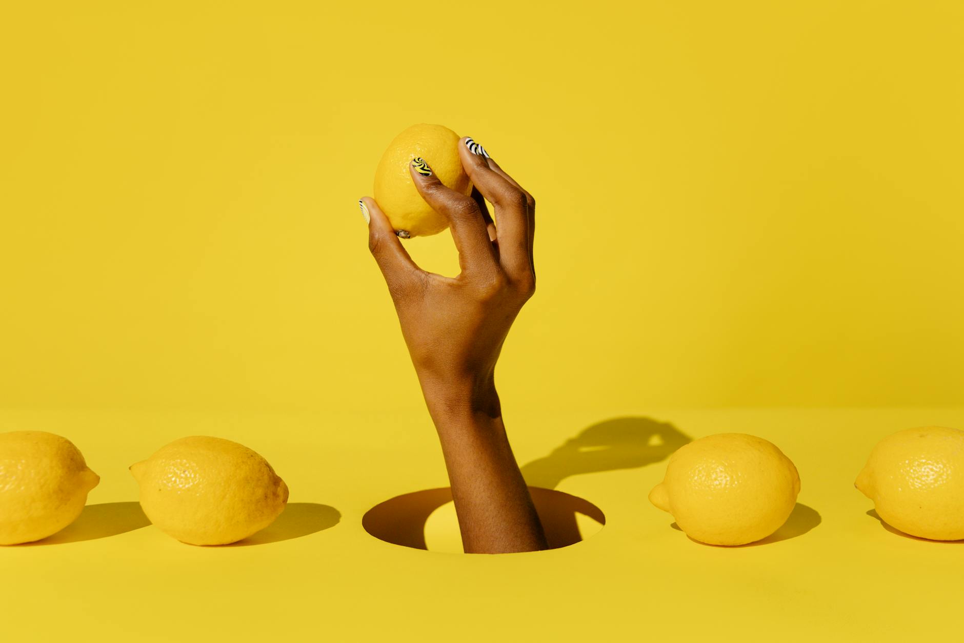 Hand holding a fresh lemon against a bright yellow background, symbolizing the gentle yet effective nature of lemon vibrators