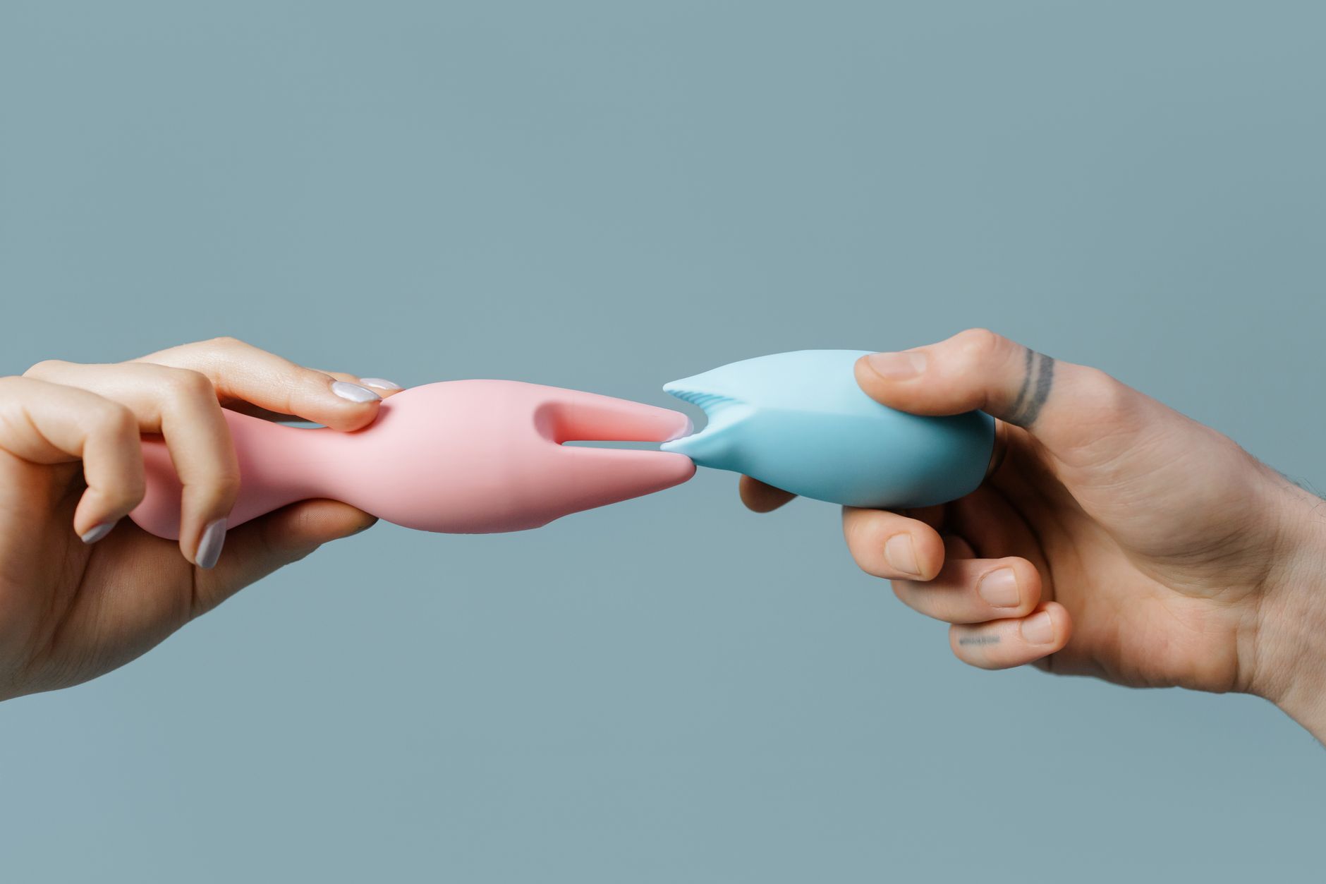 Hands holding pastel-colored silicone pleasure toys for adult wellness