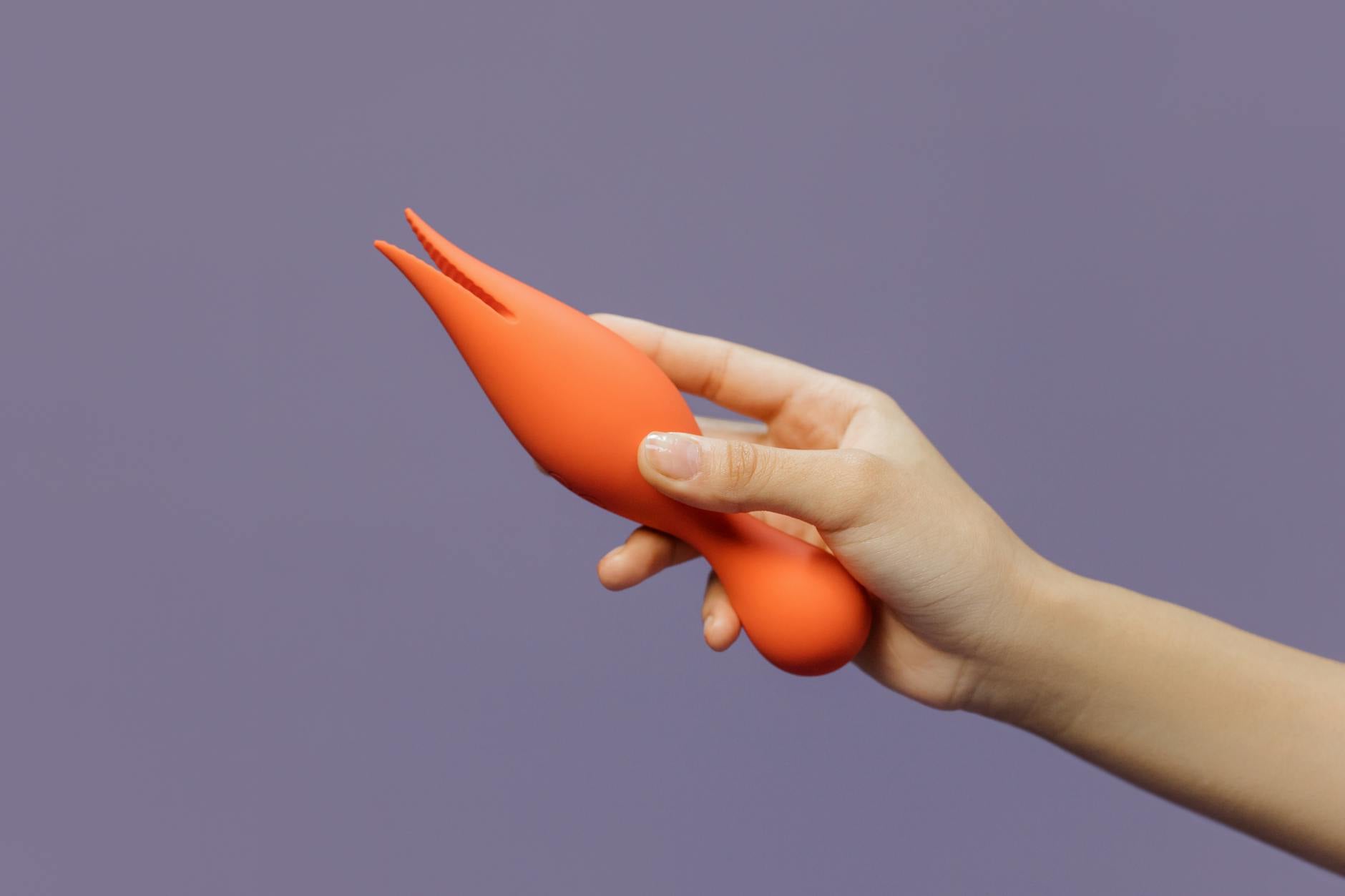 Close-up of a hand holding a vibrator against a minimalistic purple backdrop, showcasing modern sensuality and intimate wellness.