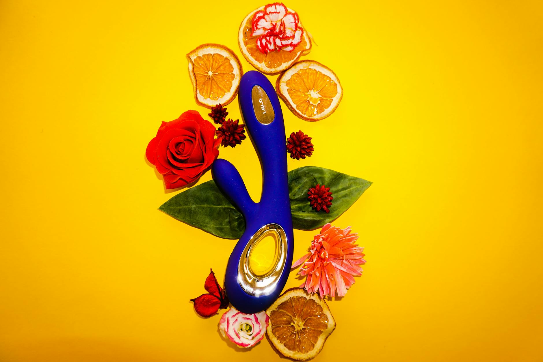 Lemon clitoral vibrator surrounded by fresh flowers and citrus slices on a bright yellow background